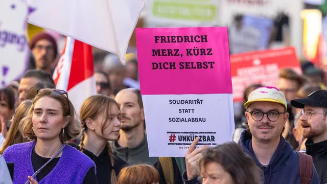 Protestatari cu pancarta roz „Friedrich Merz, kürz dich selbst” și mesajul „Solidarität statt Sozialabbau”
