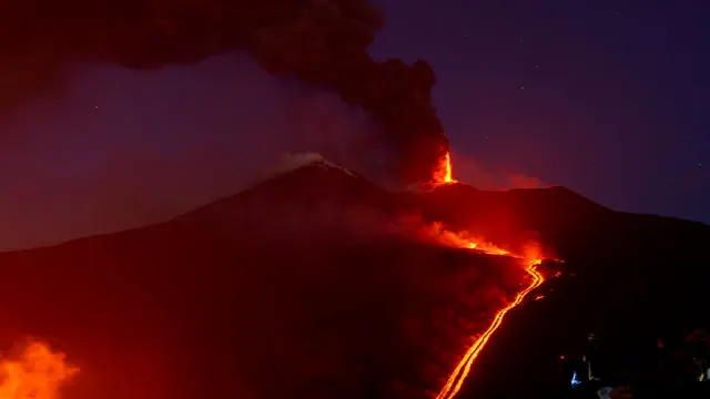 Erupție vulcanică noaptea, cu un râu de lavă incandescentă coborând pe versantul muntelui