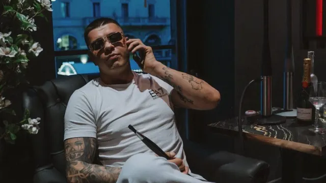 Bratan, cu ochelari de soare și brațe tatuate, vorbind la telefon pe o canapea