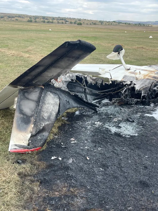 Epava carbonizată a unui avion ușor, pe un teren cu iarbă