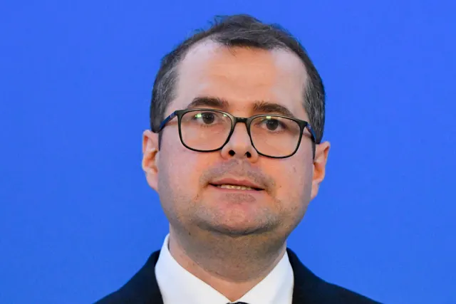 Bărbat cu ochelari și sacou închis, pe un fundal albastru