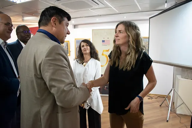 Bărbat în sacou bej dând mâna cu o femeie, într-o sală cu ecran de proiecție, la vizionarea „Tânărul Washington”