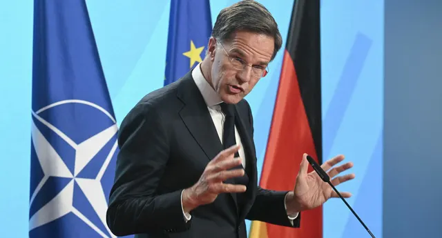 Mark Rutte gesticulând la un pupitru, în fața drapelelor NATO, UE și Germaniei
