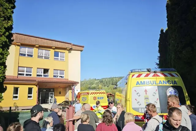 Ambulanțe și oameni adunați în fața unei școli cu fațada galbenă, sub cer senin