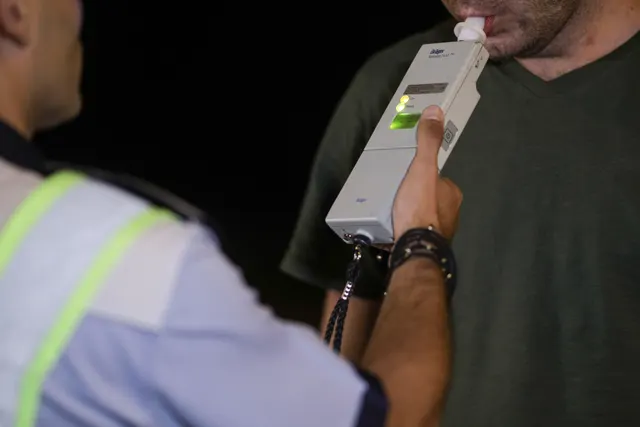 Bărbat suflând într-un etilotest ținut de un agent în vestă reflectorizantă