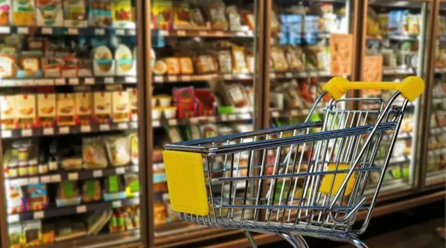 Cărucior de cumpărături cu mâner galben pe culoarul unui supermarket, între rafturi pline