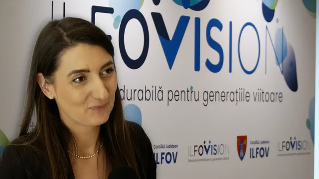 Femeie cu părul lung, șaten, zâmbind în fața panoului Ilfovision al Consiliului Județean Ilfov