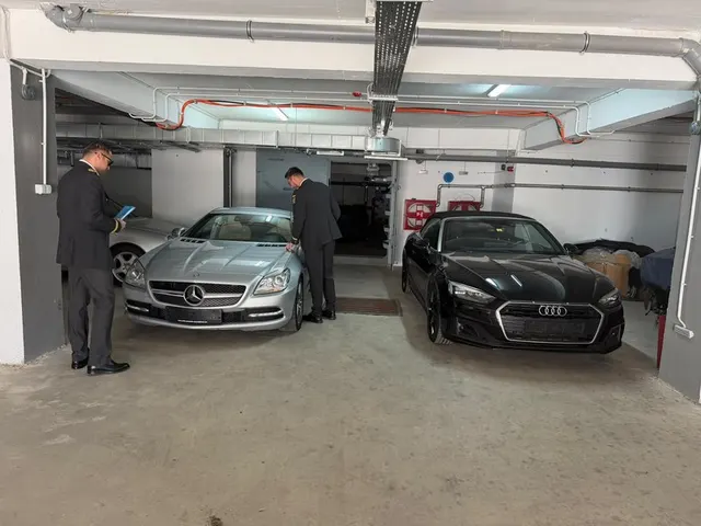 Două autoturisme de lux, unul argintiu și unul negru, într-o parcare subterană, cu doi bărbați lângă ele