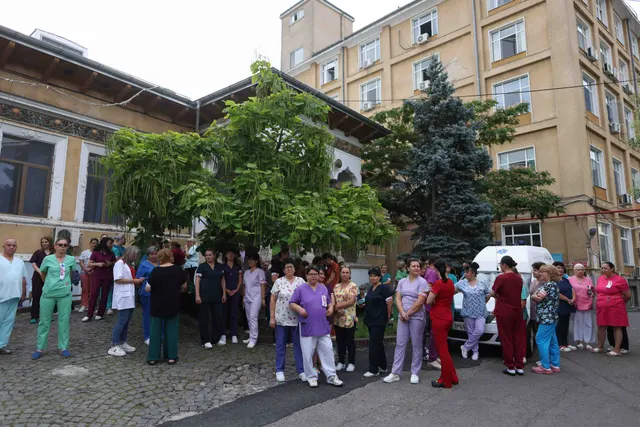 Grup de oameni, unii în uniforme medicale, adunați în curtea din fața unei clădiri cu etaje