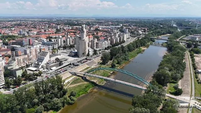 Vedere aeriană a unui oraș traversat de un râu, cu poduri, blocuri și spații verzi pe maluri