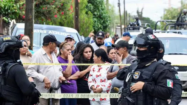 Polițiști în echipament tactic, unul cu drapelul Mexicului pe mânecă, lângă o mulțime oprită de o bandă