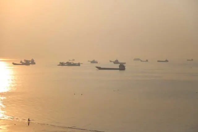 Mai multe nave pe mare, în lumina aurie și ceața dimineții, cu soarele reflectat în apă
