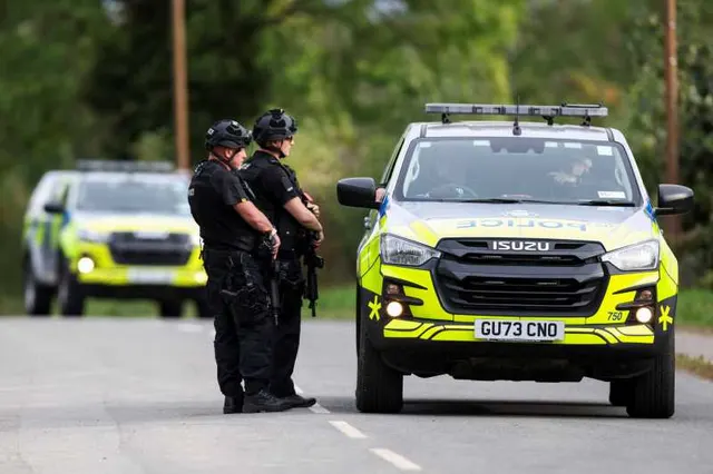 Doi polițiști înarmați lângă mașini de poliție cu marcaj galben-verde, pe un drum