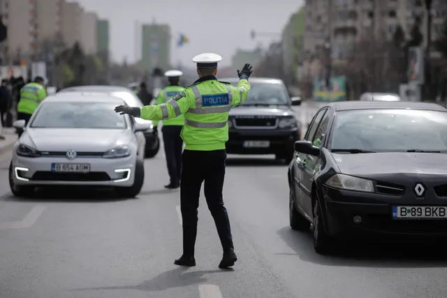 Polițist rutier în vestă galbenă dirijând circulația, cu mașini oprite pe un bulevard