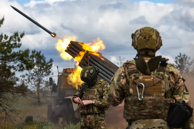 Militari în echipament de luptă lângă un lansator multiplu de rachete care trage, cu flăcări și fum