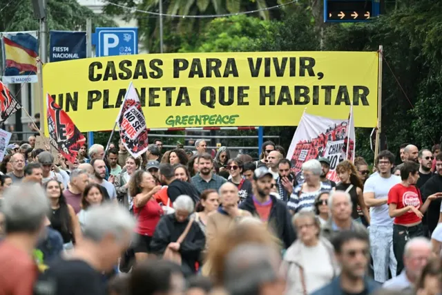 Mulțime la un protest, sub un banner galben Greenpeace: „Casas para vivir, un planeta que habitar”