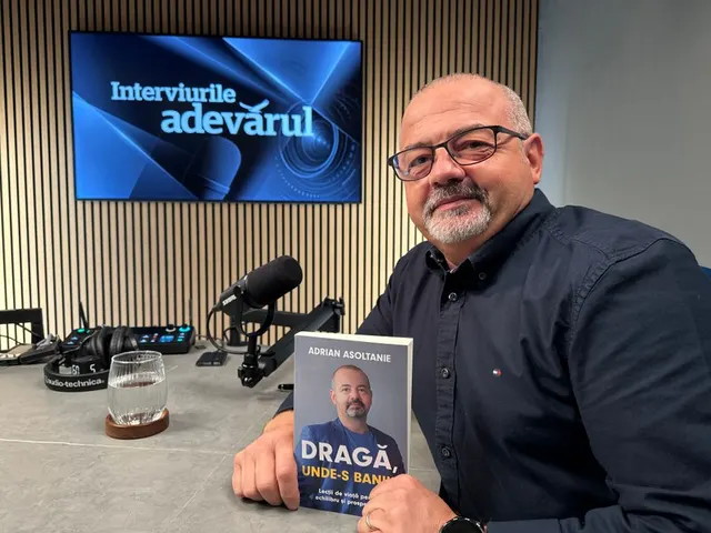 Bărbat cu ochelari și barbă, ținând o carte, într-un studio cu ecranul „Interviurile Adevărul”