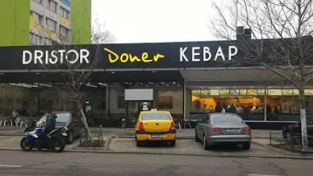 Fațada unui restaurant Dristor Doner Kebap, cu un taxi galben și mașini parcate în față