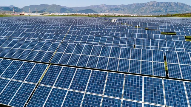 Rânduri lungi de panouri fotovoltaice, cu un lanț de munți în fundal