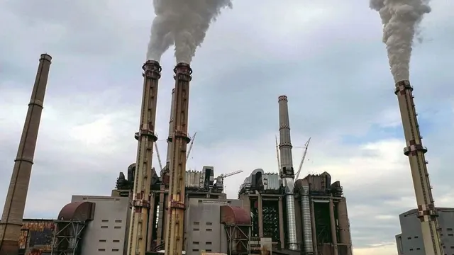 Coșurile unei termocentrale scoțând fum, sub un cer înnorat