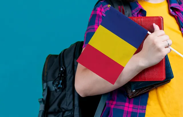 Elev în cămașă în carouri, cu rucsac, ținând un steag al României și un caiet roșu