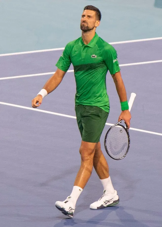 Jucător de tenis în tricou și șort verzi, cu racheta în mână, pe un teren cu suprafață albastră