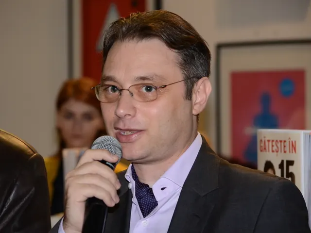 Luca Niculescu, cu ochelari și sacou închis, vorbind la microfon în fața unor afișe