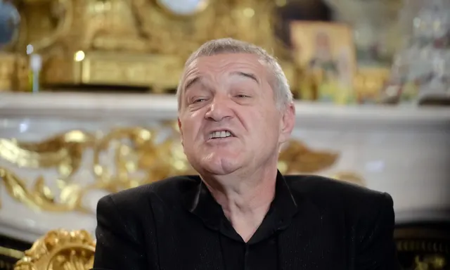 Bărbat cu părul cărunt, în pulover negru, vorbind într-o încăpere cu ornamente aurite