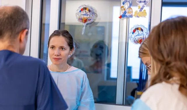 Femeie în halat de protecție bleu, într-o secție de spital decorată cu baloane, discutând cu personalul
