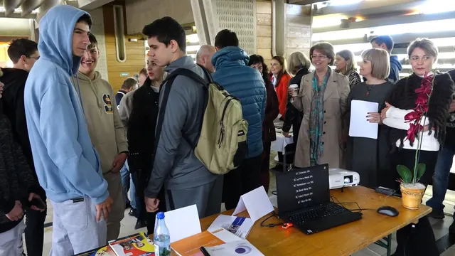 Tineri la o bursă a locurilor de muncă, în fața meselor unde angajatorii le prezintă ofertele