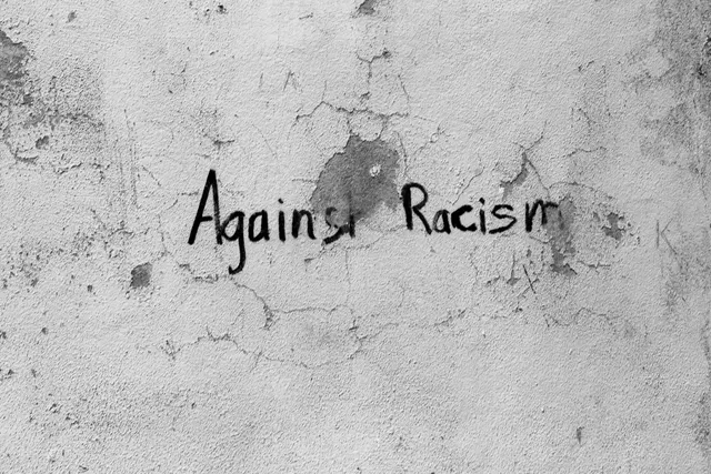 Inscripția „Against Racism” scrisă cu negru pe un perete alb crăpat