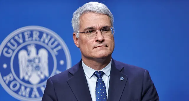 Dragoș Pîslaru, cu ochelari, în costum închis, în fața emblemei Guvernului României