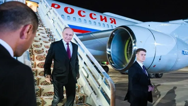 Bărbat în palton închis coborând scara unui avion cu inscripția „Россия”, pe un covor roșu