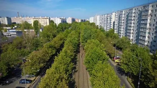 Bulevard larg cu șiruri de copaci și linii de tramvai, mărginit de blocuri înalte, văzut de sus
