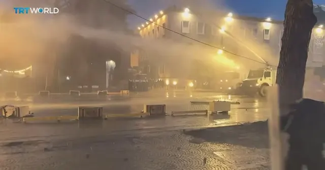 Captură TRT World: o stradă luminată noaptea, învăluită în fum, cu obiecte aruncate pe carosabil