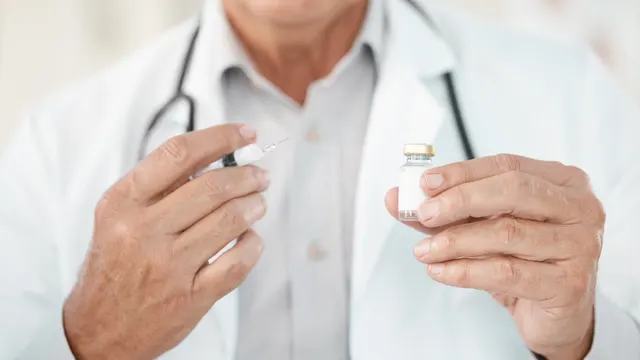 Medic în halat alb, cu stetoscop, ținând o seringă și un flacon de vaccin