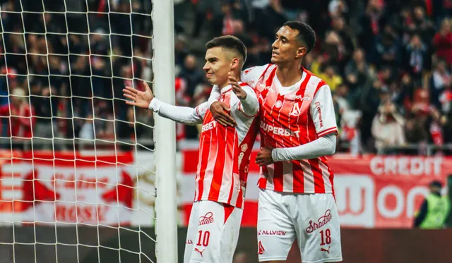 Doi fotbaliști în tricouri roș-albe, cu numerele 10 și 18, se bucură lângă poartă
