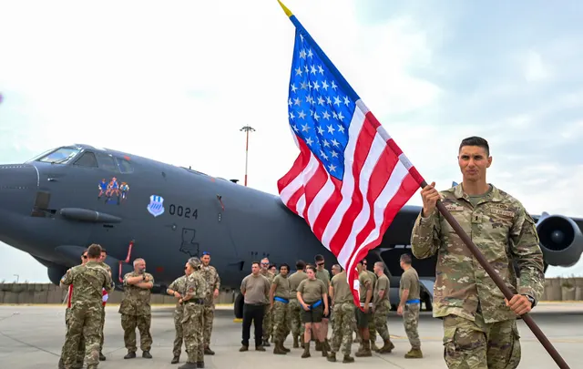 Militari americani în uniforme de camuflaj lângă un avion militar mare, unul dintre ei ținând drapelul SUA