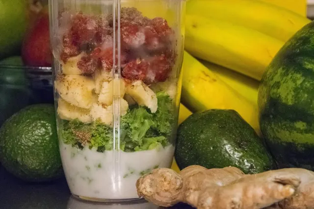 Blender plin cu fructe și verdețuri pentru un shake, lângă banane, avocado, ghimbir și pepene