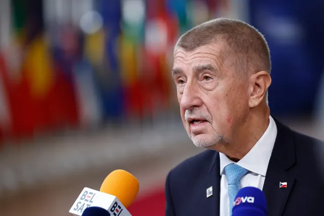 Bărbat în vârstă, cu părul cărunt, vorbind la microfoanele presei, cu drapele europene în fundal