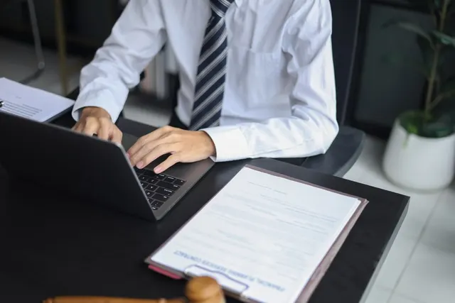 Bărbat în cămașă albă și cravată, scriind la laptop lângă un document, la un birou