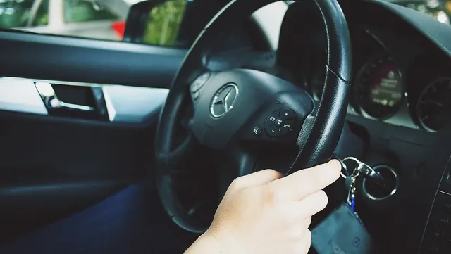 Mână care introduce cheia în contactul unei mașini Mercedes, lângă volanul cu sigla mărcii