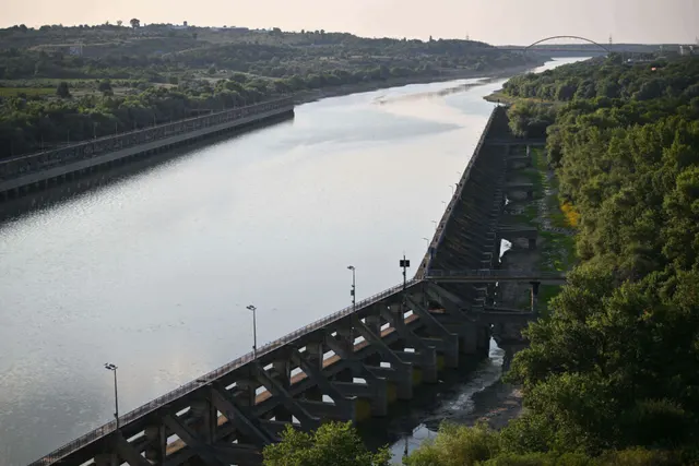 Canal larg cu apă, mărginit de un dig de beton și de pădure, fotografiat de sus