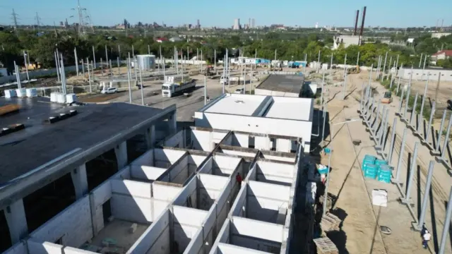 Șantier văzut de sus, cu fundațiile și pereții de beton ai unei hale în construcție, lângă o zonă industrială