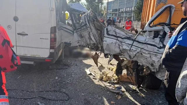 Microbuz alb distrus după un accident rutier, cu resturi pe asfalt și salvatori lângă epavă