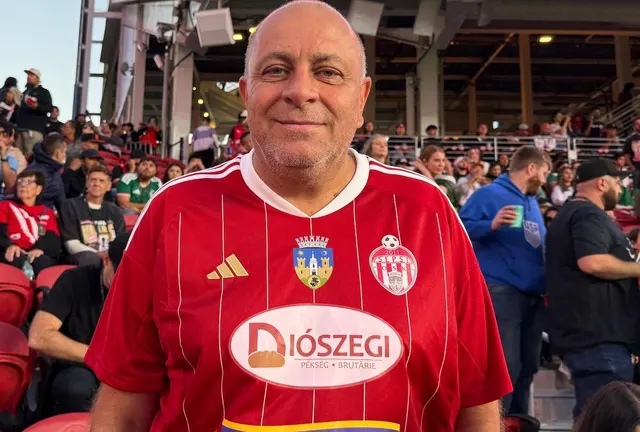Bărbat chel, zâmbitor, în tricou roșu de fotbal cu sigla sponsorului Diószegi, în tribuna unui stadion