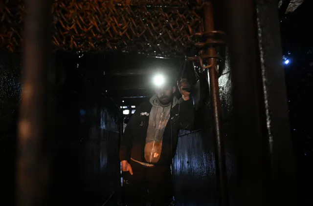 Miner cu lanterna de cască aprinsă, într-o galerie întunecată de mină